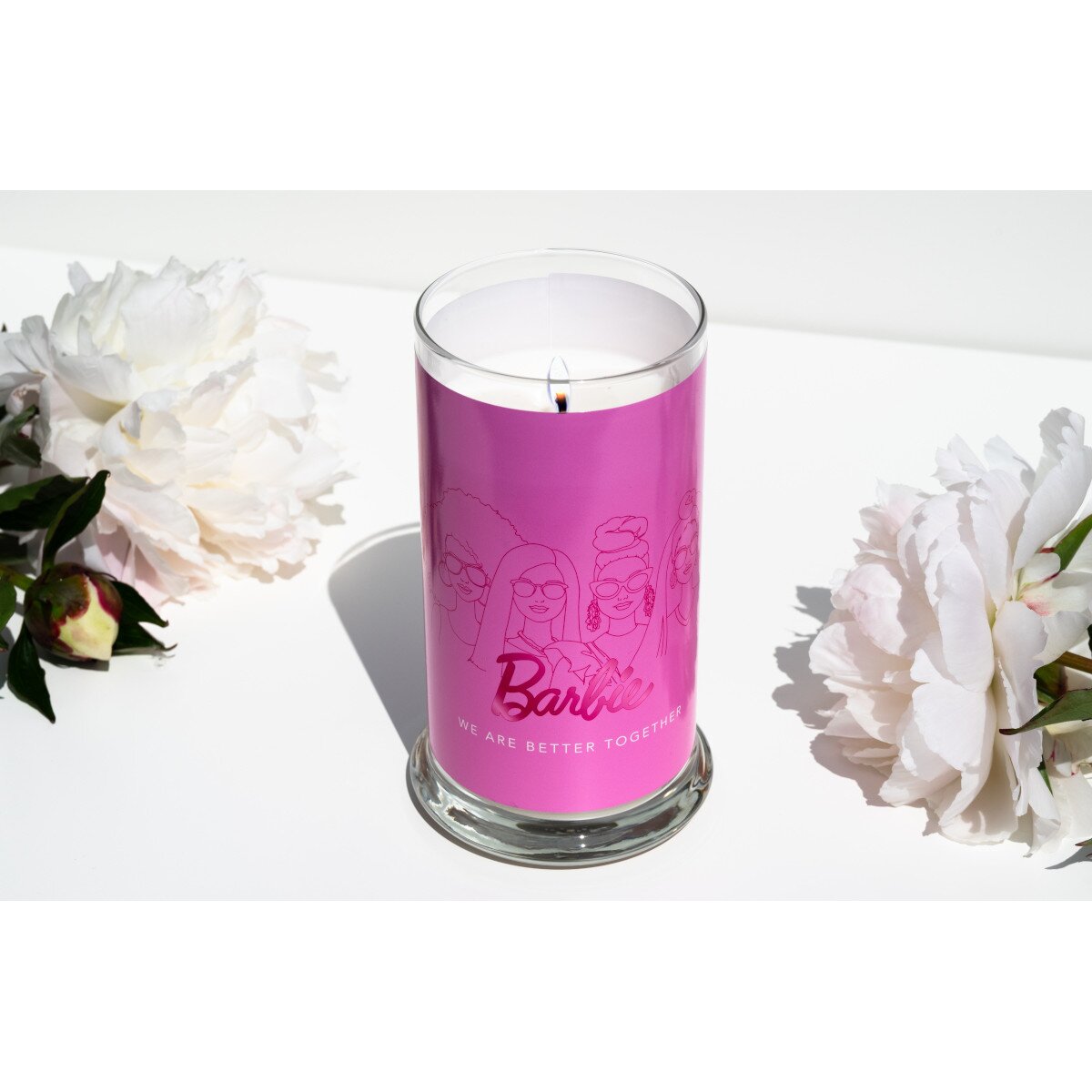 Moodbild der Barbie Duftkerze ‚Better Together‘ (400g) – geöffnetes pinke Glas mit brennendem Docht und zwei weißen Blumen. Sojawachskerze als Deko oder Geschenkidee für Barbie-Fans.