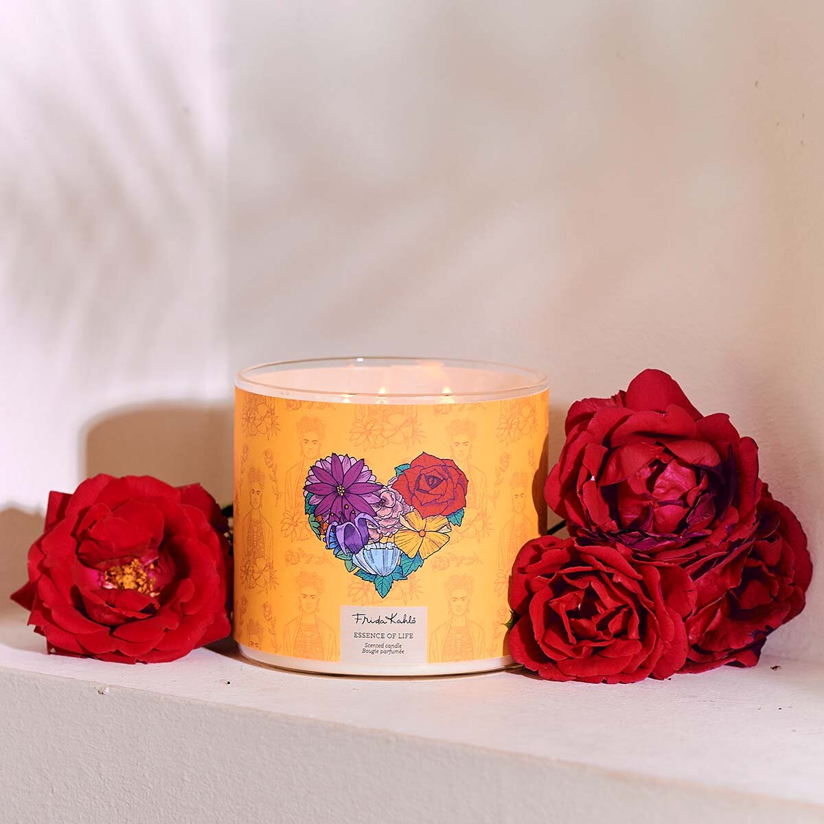 Frida Kahlo Duftkerze ‚Essence of Life‘ (400g) – Moodbild der offiziellen Lizenzkerze ohne Deckel und mit Blick auf die drei Baumwolldochte und mit Rosendeko. Romantische Duftkerze im Glas, perfekt als Geschenk zum Valentinstag.