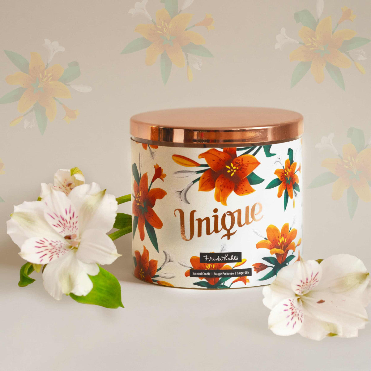 Frida Kahlo Duftkerze ‚Unique‘ (400g) – Moodbild der offiziellen Lizenzkerze im blumigen Design. Die kunstvoll verzierte Kerze steht frontal auf einem weißen Untergrund, links und recht von ihr liegen weißen Blumen – dekoratives Wohnaccessoire und ideale Geschenkidee für unter 20 € für Duftkerzen-Liebhaber.
