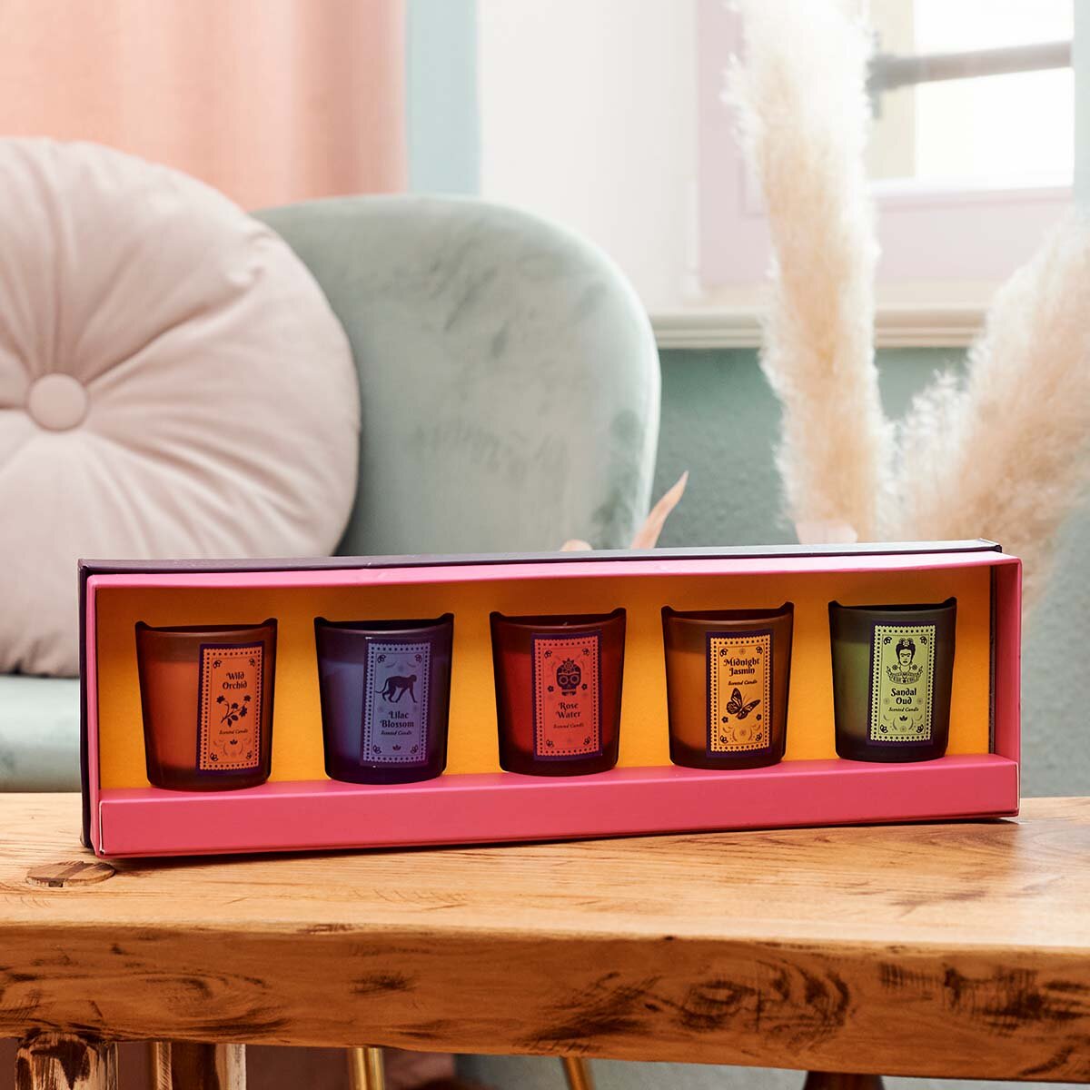 Frida Kahlo Geschenkeset ‚Garden of Scents‘ (5x45 g) - offener Geschenkkarton des Frida Kahlo Sets ‚Garden of Scents‘ auf einem Holztisch. Im Hintergrund sieht man ein grünes Sofa. Die Kerzen des Sets sehen sehr hochwertig aus.