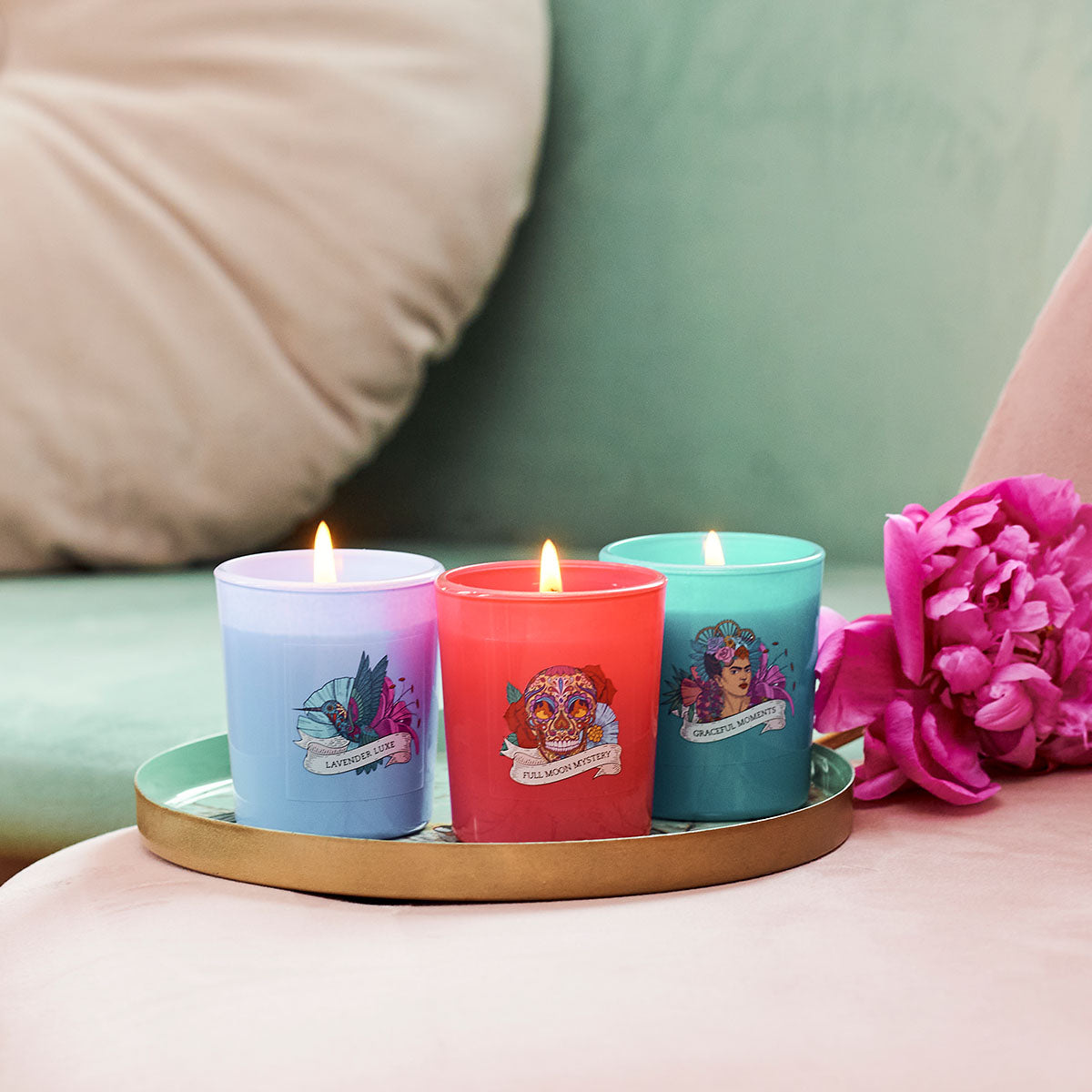 Frida Kahlo Geschenkeset ‚Quiet Moment‘ (3x70 g) - Die drei brennenden Kerzen stehen auf einem goldenen Teller neben einer rosa Blüte. Die stilvollen Duftkerzen mit einzigartigen Aromen sind ein dekorativer Blickfang und kreatives Geschenk für Kunst- und Duftliebhaber.