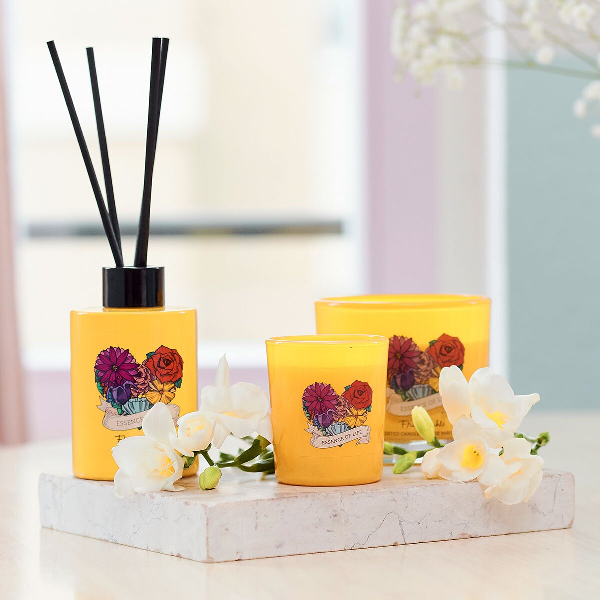 Frida Kahlo Essence of Life Kollektion Duftstäbchen zusammen mit Duftkerzen. Stilvoll angerichtet auf einem Mamorstein mit weißen Blüten. Perfekte Raumerfrischer, die eine elegante und hochwertige Dekoration darstellen.