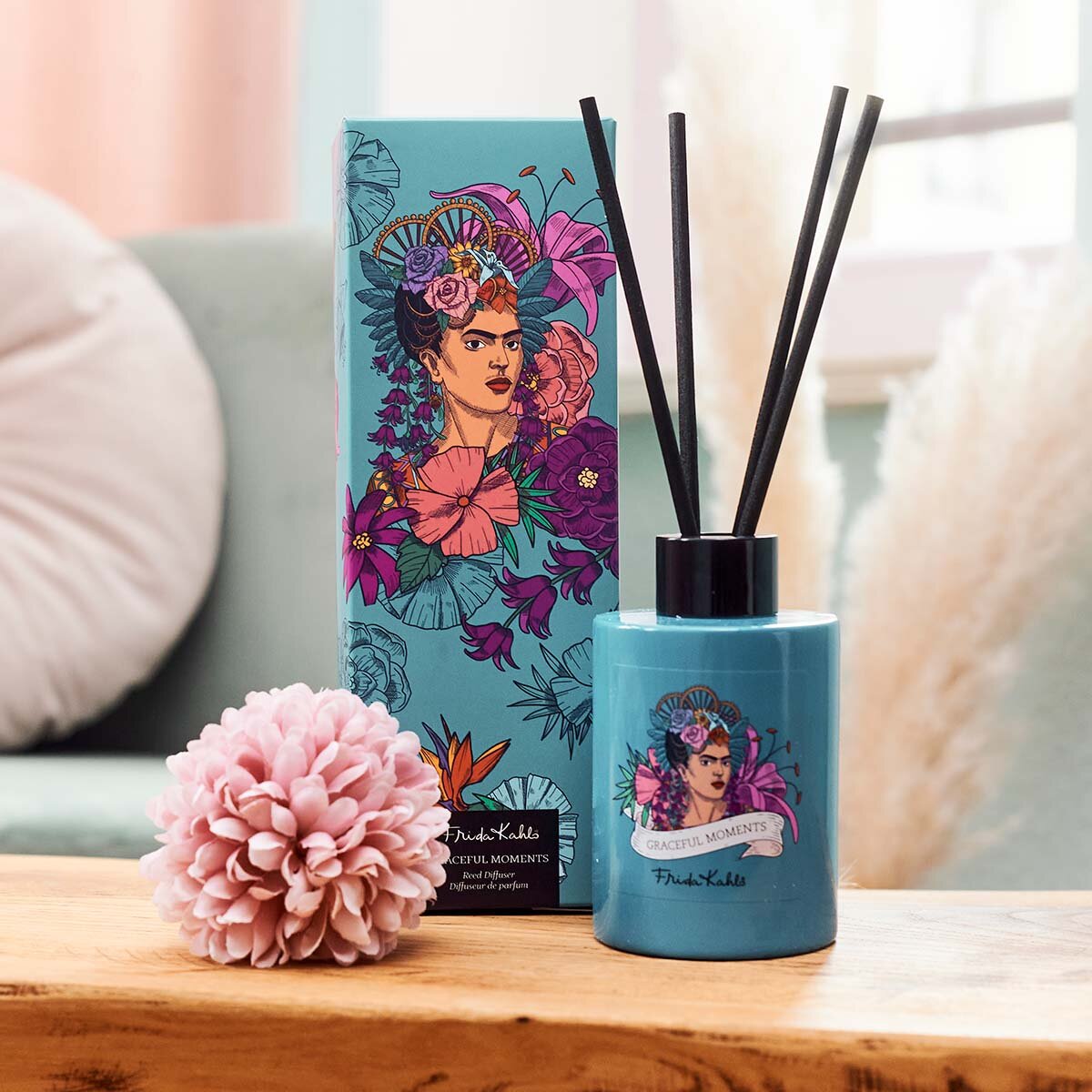 Frida Kahlo Graceful Moments Duftstäbchen zusammen mit Geschenkkarton. Stilvoll angerichtet im Wohnzimmer auf einem Holztisch mit einer rosa Blüte. Perfekte Raumerfrischung, die eine elegante und hochwertige Dekoration darstellen