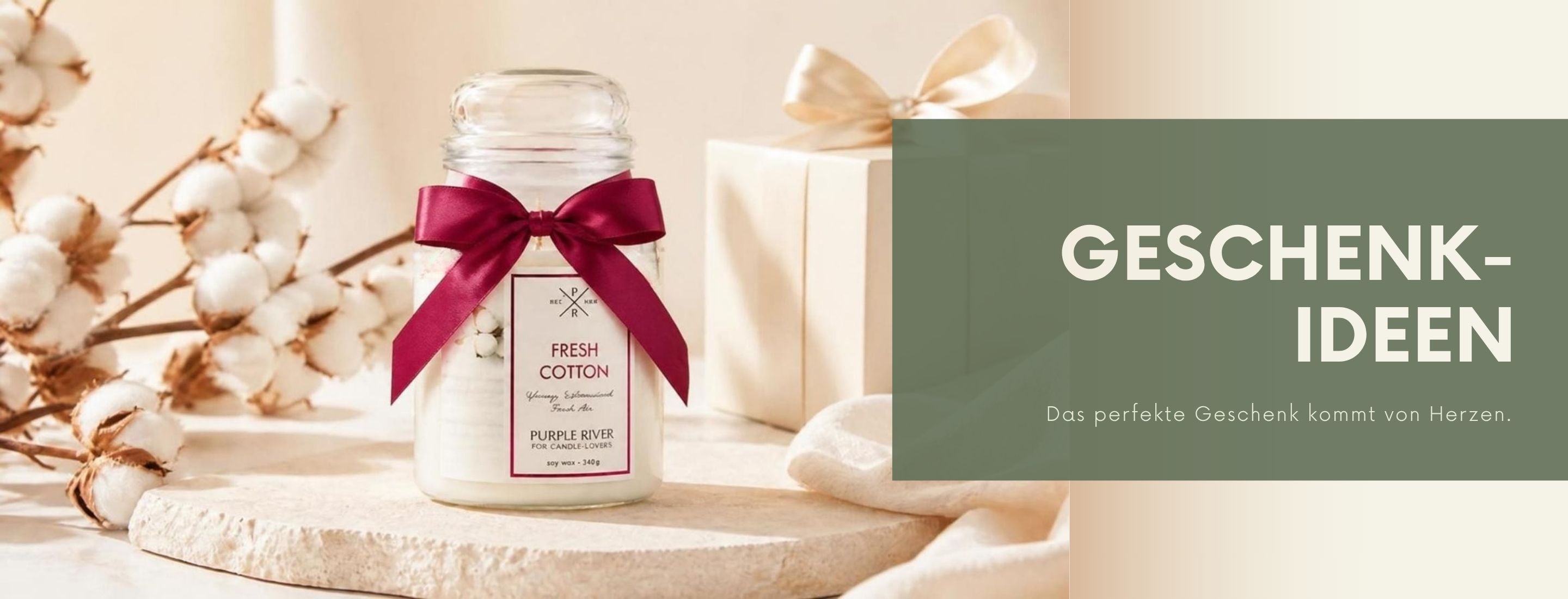 CandleVibes Geschenkideen: Eine Purple River Fresh Cotton Duftkerze mit roter Schleife, arrangiert mit einer hellen Geschenkbox und Baumwollblüten. Liebevoll dekorierte Duftkerze im Glas als Geschenkidee für jeden Anlass.