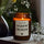 mad candle Duftkerze aus Sojawachs mit dekorativen Etikett, Teelicht und Blume im Hintergrund. Die Kerze brennt und steht auf einem Buch.
