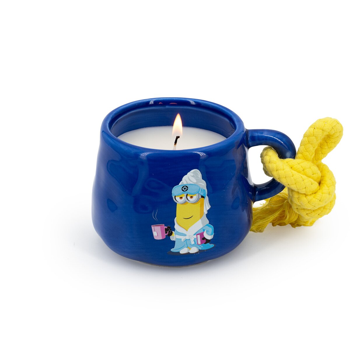 Minions Duftkerze Kevin (200g) in blauer Keramiktasse mit gelber Kordel. Als Motiv sieht man den Minion Kevin im Bademantel, der in der einen Hand Buch hält und in der anderen eine Tasse Tee.  Das Wachs ist weiß und der Docht brennt.