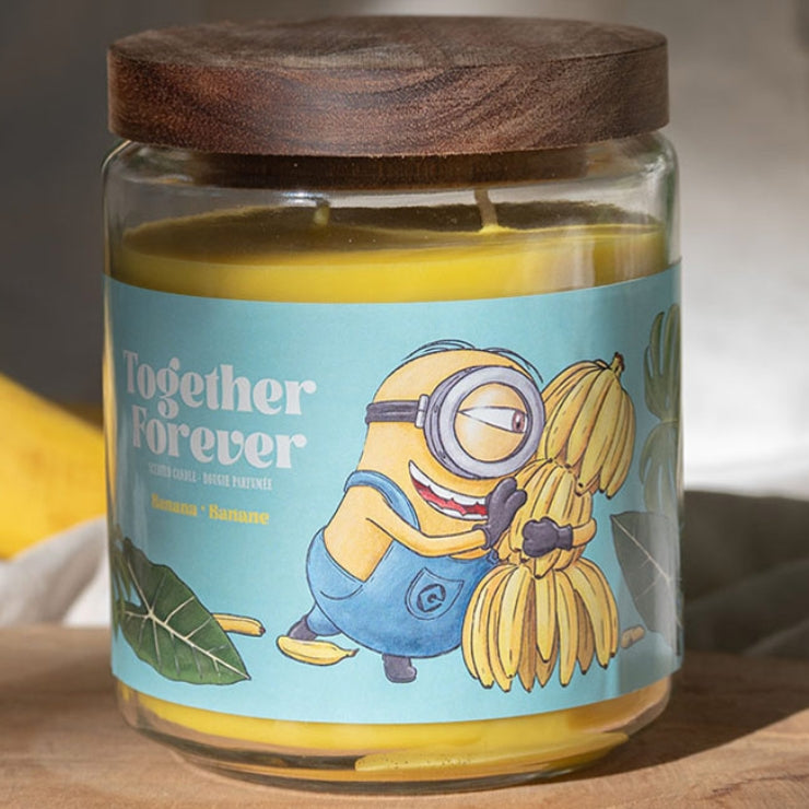 Minions XXL-Duftkerze ‚Together Forever‘ (510g) – Moodbild der offiziellen Lizenzkerze mit farbenfrohem Minions-Motiv, Palmenblättern und einer Bananenstaude. Vegane Duftkerze im Glas als stylische Deko oder Geschenk für Fans.