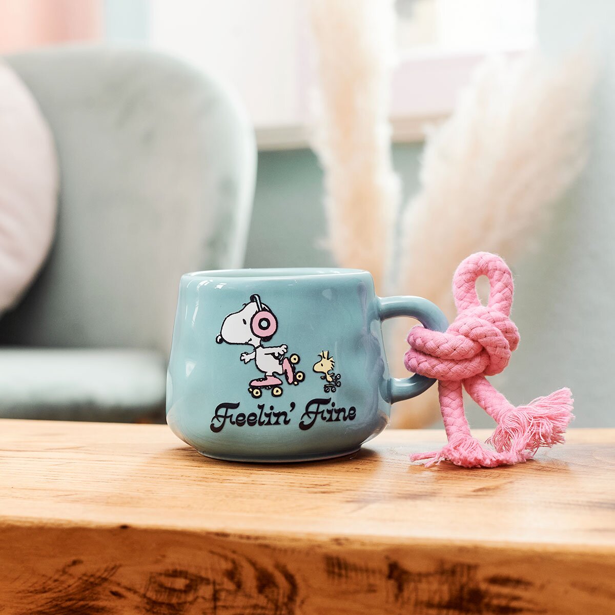 Peanuts-Duftkerze Feeling Fine (275g) in türkisfarbener Keramiktasse mit Snoopy und Woodwick Motiv. Moodbild der Tassen, die in einem gemütlichen und dekorativen Wohnzimmer steht