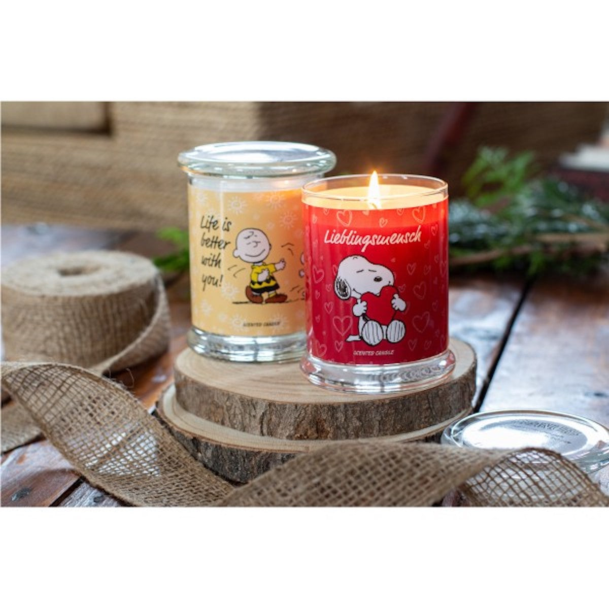Peanuts Duftkerzen ‚Lieblingsmensch‘ (250 g) und ‚Life is better with you‘ (250g) - Moodbild. Die zwei hochwertigen Duftkerzen im Glas für eine romantische Atmosphäre und ein gemütliches Zuhause stehen auf einer Holzscheibe. Eine brennt, die andere nicht.