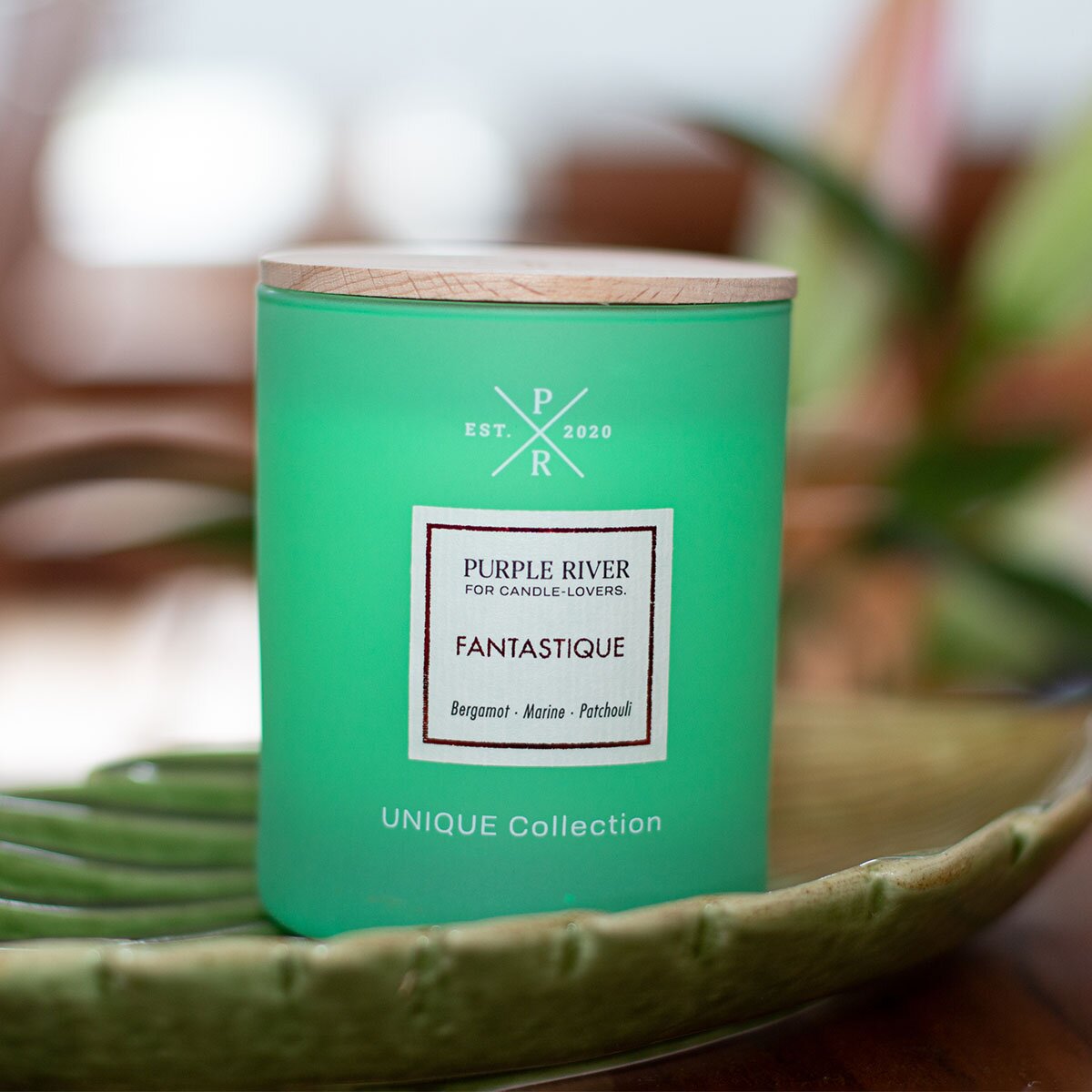 Nachhaltige Premium-Duftkerze von Purple River in grüne mit extralanger 140h-Brenndauer. Hochwertige Wellness-Deko im Glas und mit Holzdeckel. Made in Germany - inszeniert auf grüner Keramikschale  im Wellnessbereich.
