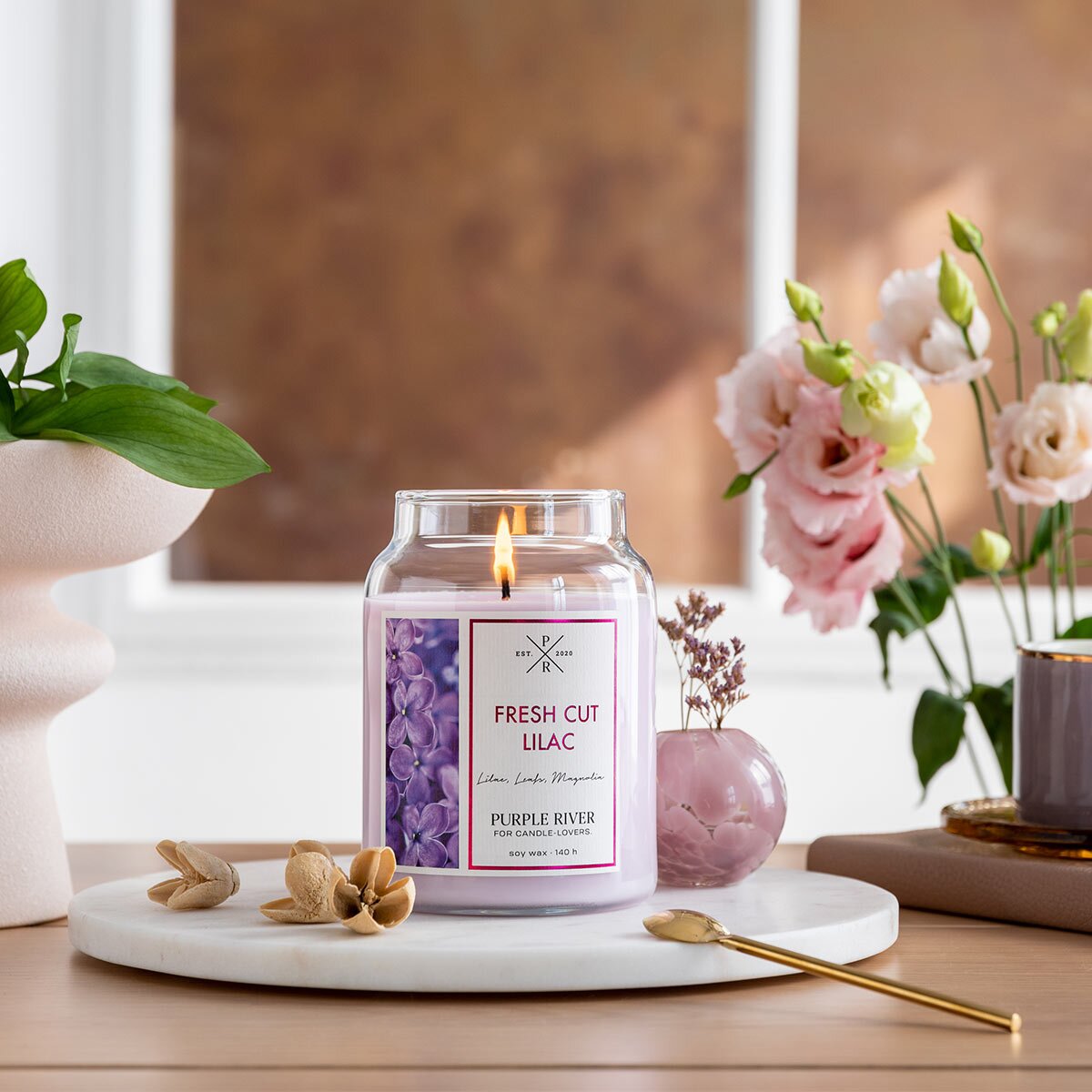 Nachhaltige Premium-Duftkerze von Purple River mit extralanger 140h-Brenndauer. Hochwertige Wellness-Deko im Glas. Made in Germany - inszeniert auf Steinplatte neben Blumen & Bucheckern im Wohnzimmer.