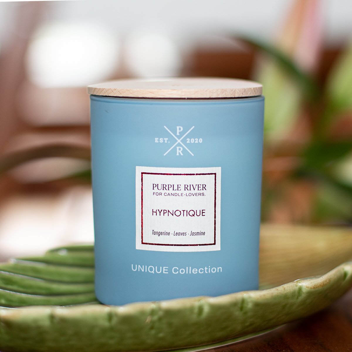 Nachhaltige Premium-Duftkerze von Purple River in blau mit extralanger 140h-Brenndauer. Hochwertige Wellness-Deko im Glas und mit Holzdeckel. Made in Germany - inszeniert auf grüner Keramikschale  im Wellnessbereich.