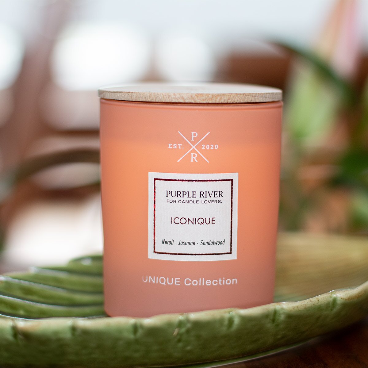 Nachhaltige Premium-Duftkerze von Purple River in orange mit extralanger 140h-Brenndauer. Hochwertige Wellness-Deko im Glas und mit Holzdeckel. Made in Germany - inszeniert auf grüner Keramikschale  im Wellnessbereich.