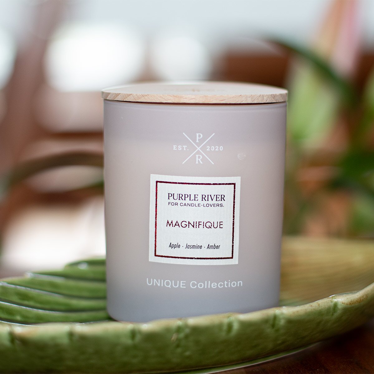 Nachhaltige Premium-Duftkerze von Purple River in rosa mit extralanger 140h-Brenndauer. Hochwertige Wellness-Deko im Glas und mit Holzdeckel. Made in Germany - inszeniert auf grüner Keramikschale  im Wellnessbereich.