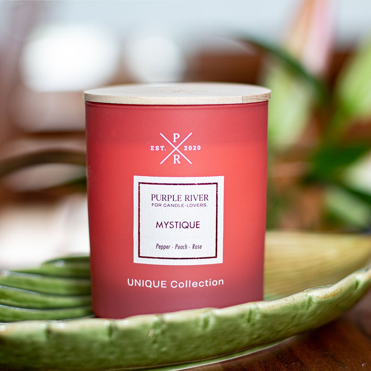 Nachhaltige Premium-Duftkerze von Purple River in rot mit extralanger 140h-Brenndauer. Hochwertige Wellness-Deko im Glas und mit Holzdeckel. Made in Germany - inszeniert auf grüner Keramikschale  im Wellnessbereich.