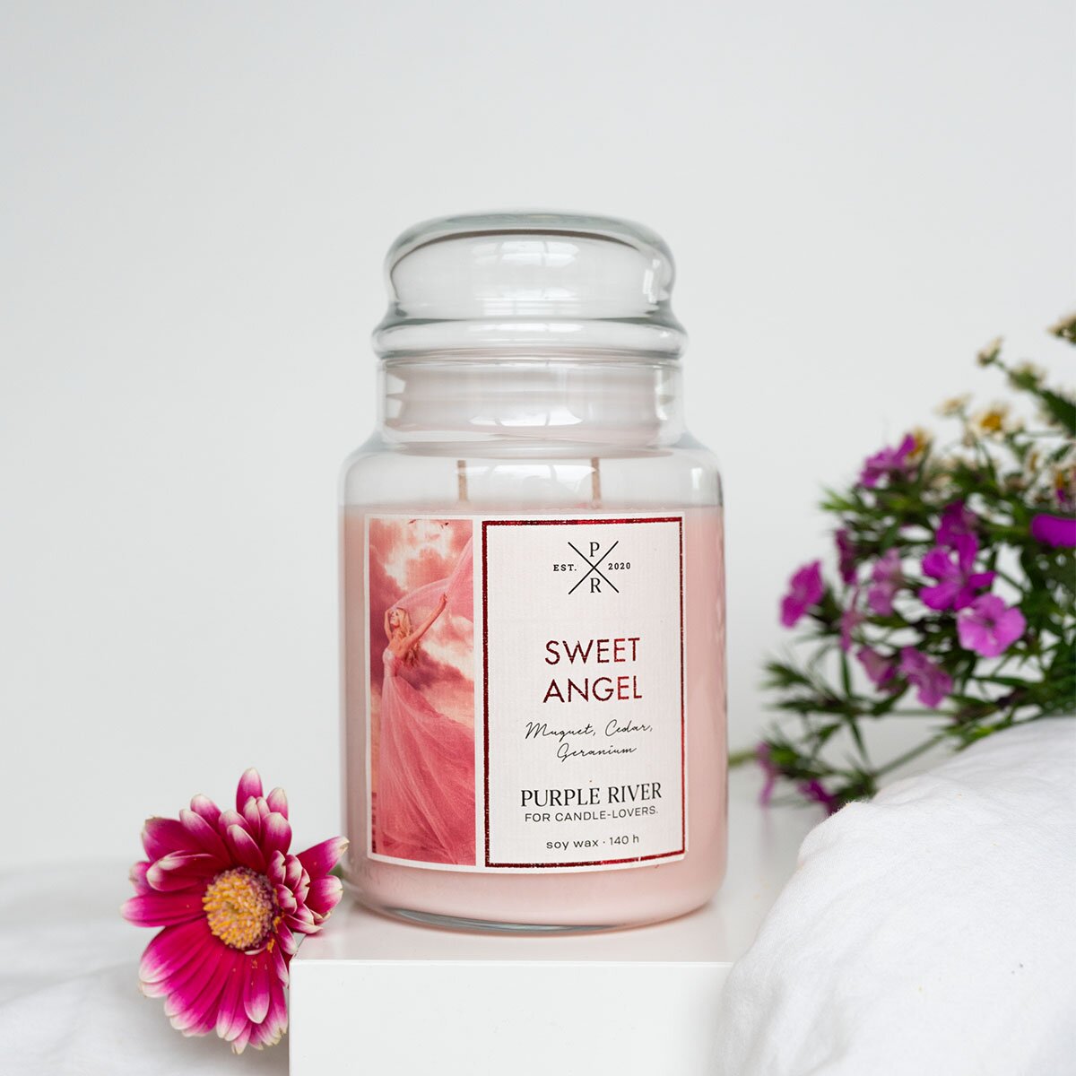 Nachhaltige Premium-Duftkerze von Purple River mit extralanger 140h-Brenndauer. Hochwertige Wellness-Deko im Glas. Made in Germany - inszeniert auf Steinplatte neben Blumen & Grünpflanzen im Badezimmer.