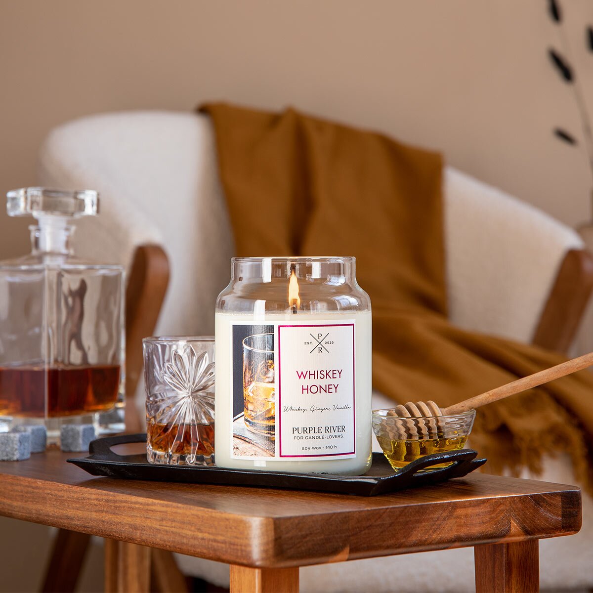 Nachhaltige Premium-Duftkerze von Purple River mit extralanger 140h-Brenndauer. Hochwertige Wellness-Deko im Glas. Made in Germany - inszeniert auf Holztisch neben Whiskey & Honig im Herrenzimmer.
